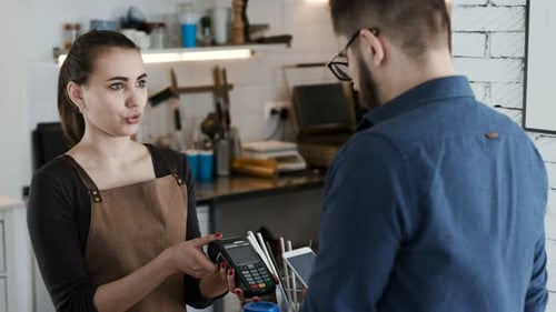 Happy young woman works at restaurant near man paying with nfc cellphone
