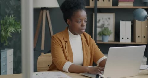 Female Entrepreneur Using Laptop Typing and Writing Business Information Working at Desk in Modern