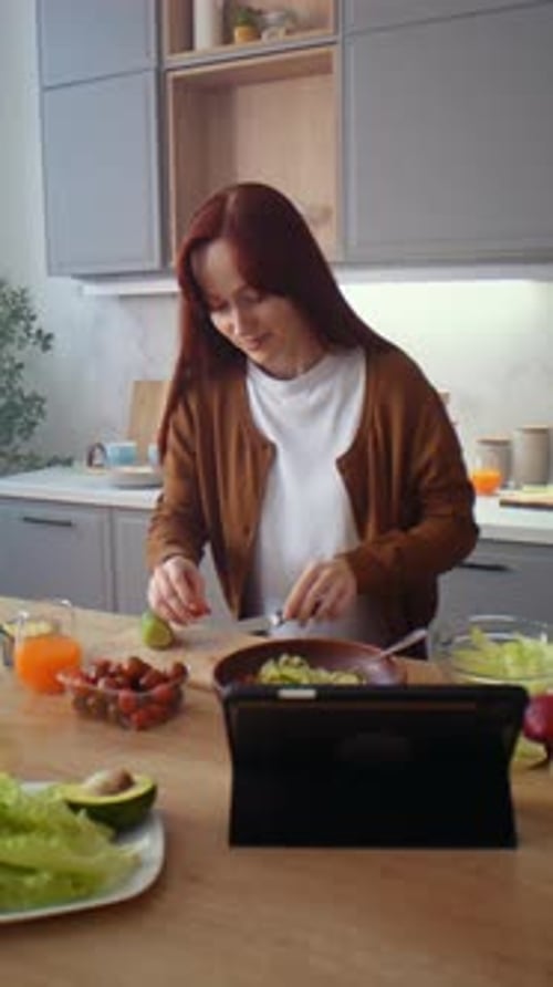 Woman Prepares Salad While Watching Tablet in Kitchen