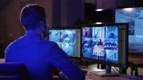 Security Guard Works on a Computer with Surveillance CCTV Video Footage in a Monitoring Center with