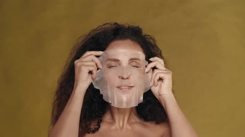 A Woman Applies a Cosmetic White Sheet Mask on Her Face Smoothes It Portrait of a Seminude Woman in