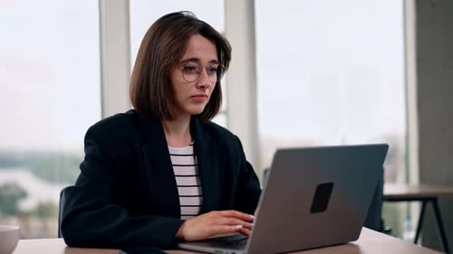 Modern good-looking young woman working in the office. Smiling lady typing on laptop.