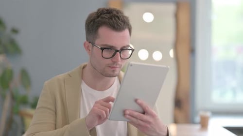 Young Adult Celebrates Success Using Tablet Indoors
