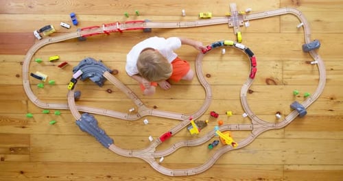 Child Plays with a Toy Train Set on Floor