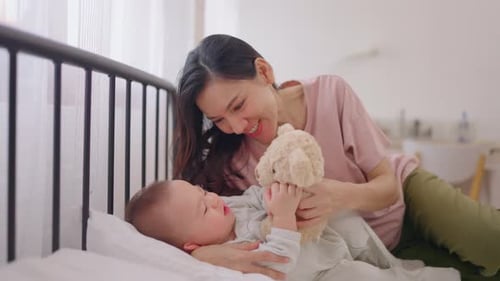 Mother Playing with Infant on Bed with Stuffed Animal