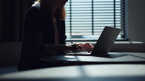 Woman in Black Suit Sitting at Office Desk and Typing Quickly on Laptop Keyboard