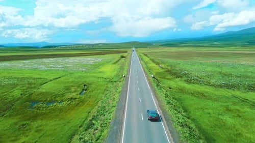 Shooting from drone shows highway among mountains of meadows. Car rushes