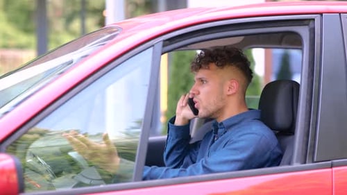 Close Up of Caucasian Young Man Sitting in Car on Driver's Seat and Talking on Smartphone in Bad