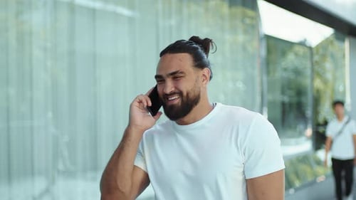 Young Man Walking on the City Street and Smiling During a Pleasant Conversation with a Friend on a