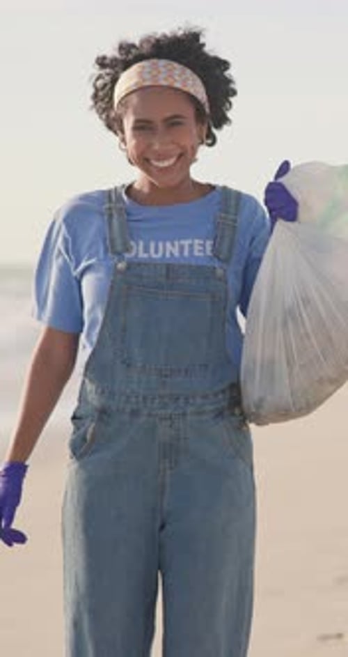 Mujer, rostro y voluntaria con una bolsa de plástico en la playa para limpiar como activista comunitaria