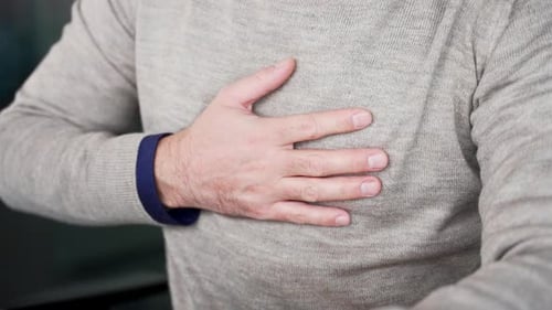Close up of male hands holding and massaging chest while sitting in modern office. Businessman