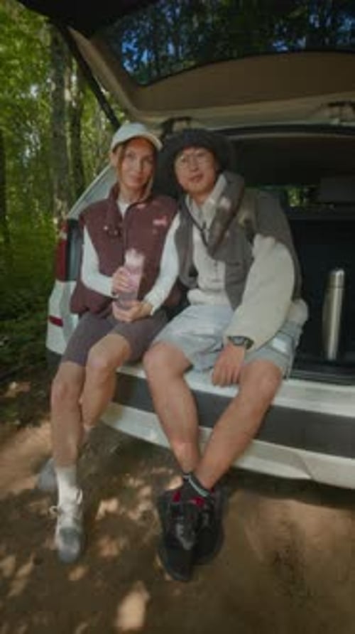 Interracial Couple Sitting on Car Trunk during Hiking Trip in Forest