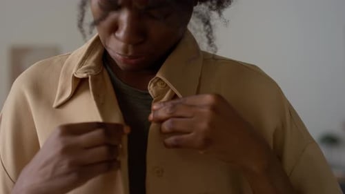 Woman Buttons Tan Colored Shirt in Indoor Setting