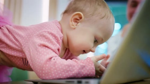 Cute Baby Interacts with Laptop on Wooden Table