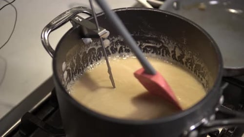 A young girl stirs a caramel mix heating up on the stove while baking millionaire shortbread cookies
