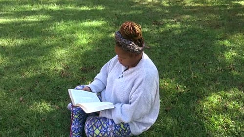 Bird's Eye view of Black woman sitting in grass reading her bible and enjoying God's natural beauty