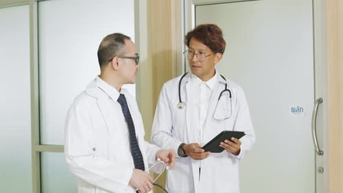 Two Asian men doctor discuss patients symptoms in hallway