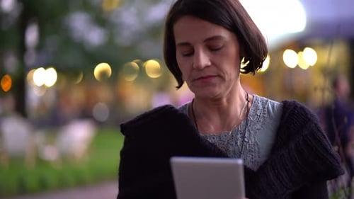 Young woman browsing on tablet in the city at night with city lights
