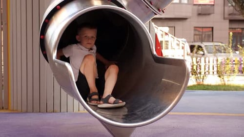 A Little Boy Rides a Metal Slide on a Playground in the Courtyard