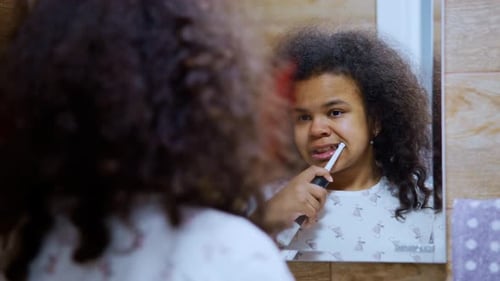 Girl with Electric Toothbrush in Bathroom Mirror