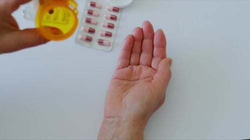 Close Up Shot of Elderly Hands Pouring Pills From an Orange Prescription Bottle Into the Palm with