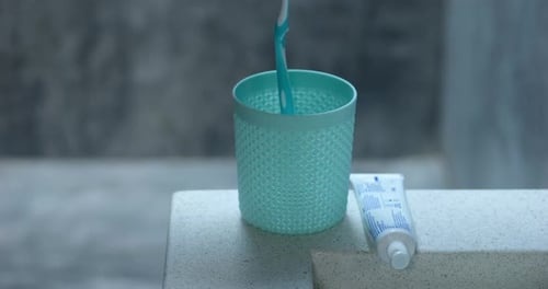 Toothbrush Falls into Cup Next to Toothpaste