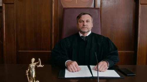 Portrait of Male Judge in Black Robe Sitting at Wooden Bench in Courtroom
