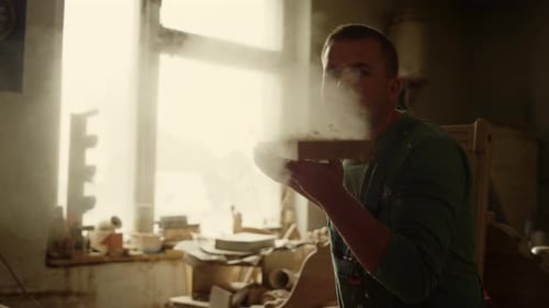 Man blowing sawdust from wooden plank in carpentry workshop craftsman portrait