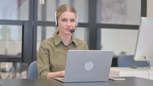 Smiling Woman Typing on Laptop with Headset in Office