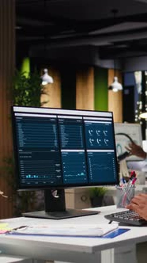 Vertical Video Office Worker Reviewing KPI Metrics on Monitor and Analytics on Desktop
