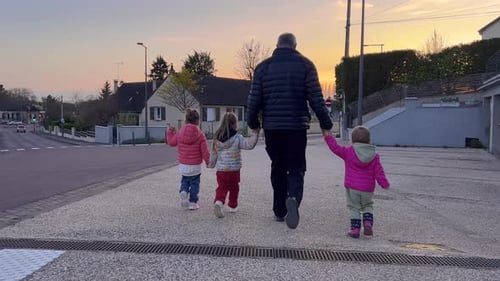 Rear View of an Elderly Dad Walking Along a City Street with Three Daughters Children are Holding