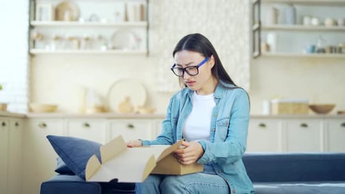 Young Adult Woman Opens Package, Looks Confused