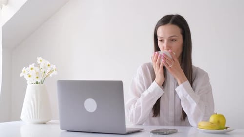 Woman with Laptop Drinks Coffee at Desk