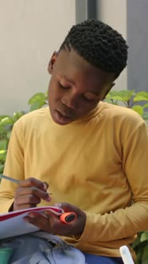 Vertical video: Inspecting page, student in yellow shirt writing notes at patio, pad, highlighter
