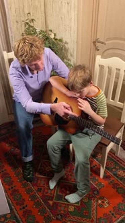 Adult Guiding Child Playing Acoustic Guitar Indoors