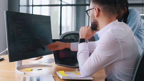 Two programmer is sitting by computer in office and working.