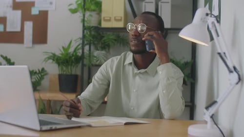 Black Businessman Talking on Phone and Making Notes in Office