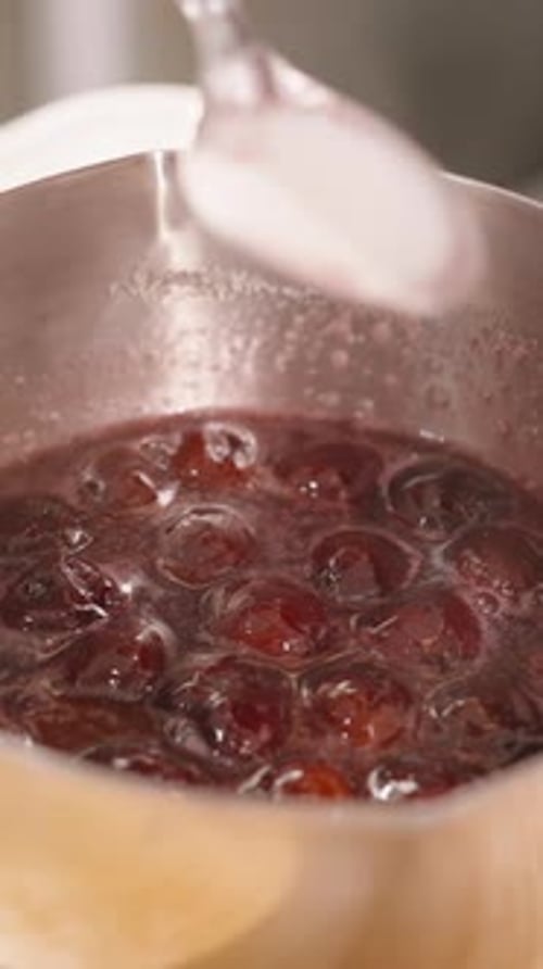 Vidéo verticale. Gros plan du liquide versé dans la sauce aux cerises fumante tout en remuant avec une cuillère