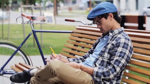 Creative young man sketching art on city street bench with fixed gear bicycle