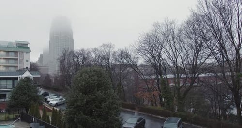A wide shot of a cloudy, dismal day with rain pouring down on a blue collar city while a tall skyscr
