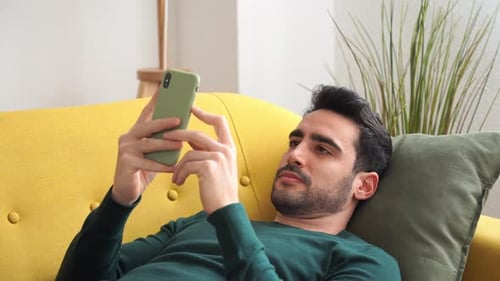 Man Relaxes, Using Smartphone on Couch Indoors