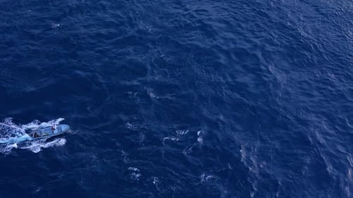 Aerial high angle overview of small fishing boat bobbing creating white wash in rocky ocean