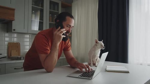 Man Talking on Phone While Using Laptop with Dog