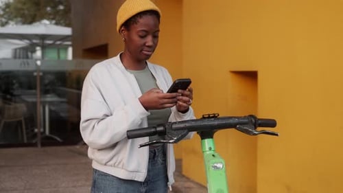 Young Woman Using Smartphone to Unlock Electric Scooter on City Street