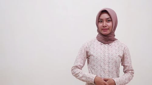 Happy young asian muslim woman standing while presenting something beside her on empty space. Isolat