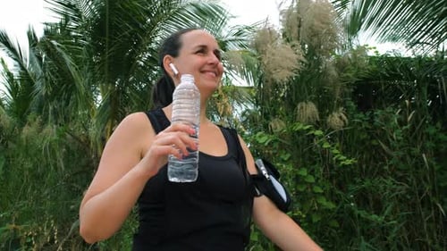 Woman Walking and Drinking Water After Workout