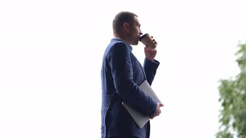 Side View of Caucasian Male Professional Holding Laptop and Drinking Coffee While Standing Outdoors