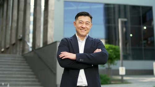 Portrait of a happy asian businessman in formal suit standing on the street near office building.
