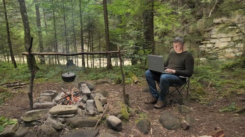 A Man Works on a Laptop in a Tourist Camp in a Beautiful Forest