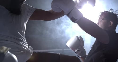Combattant repoussant son adversaire à l'intérieur du ring dans un éclairage Théâtral capturé au ralenti.
Deux
